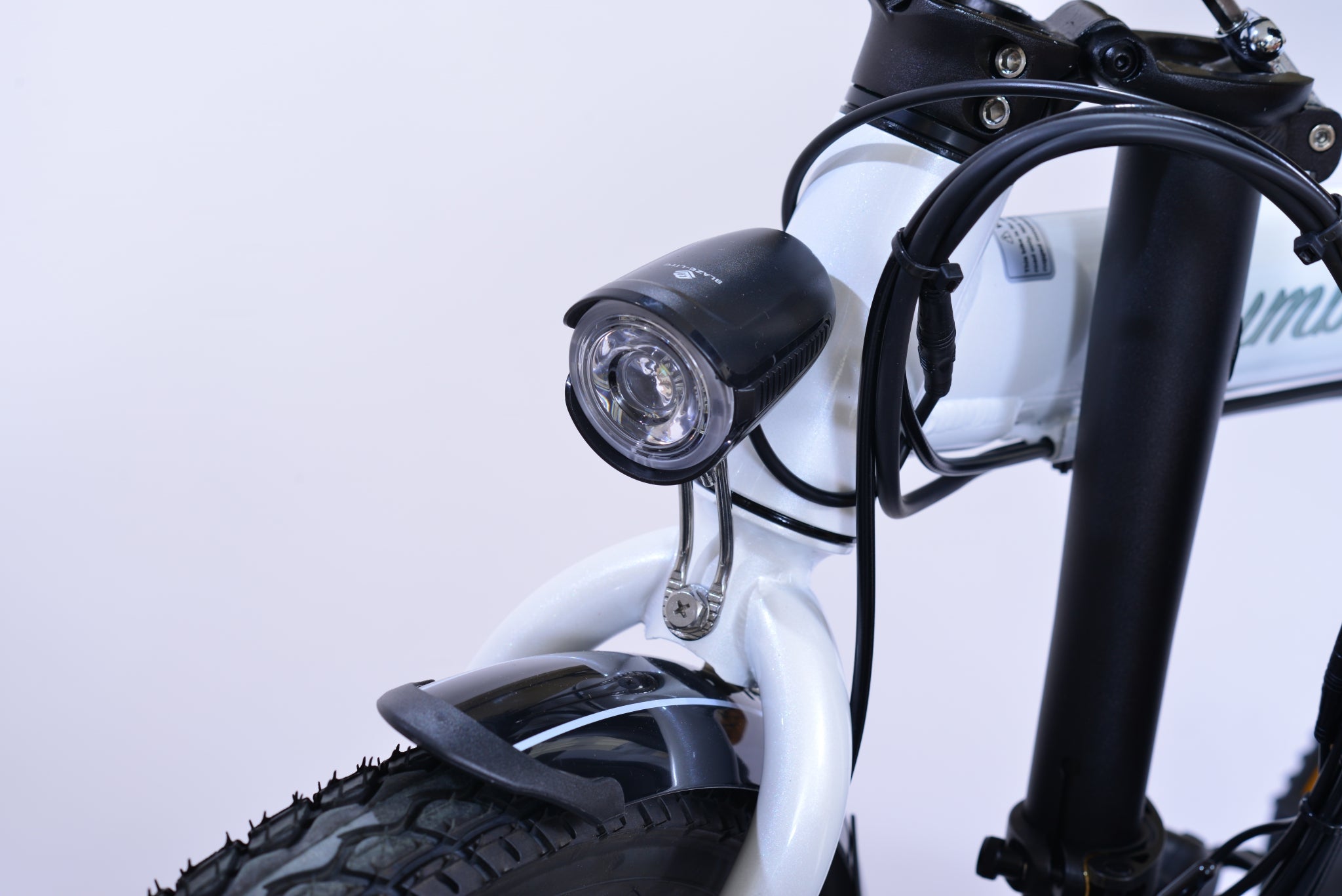 View of a headlight of a white electric folding bicycle.