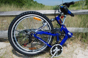 The folded position of a blue foldable bicycle at a beach location with sand and grass.
