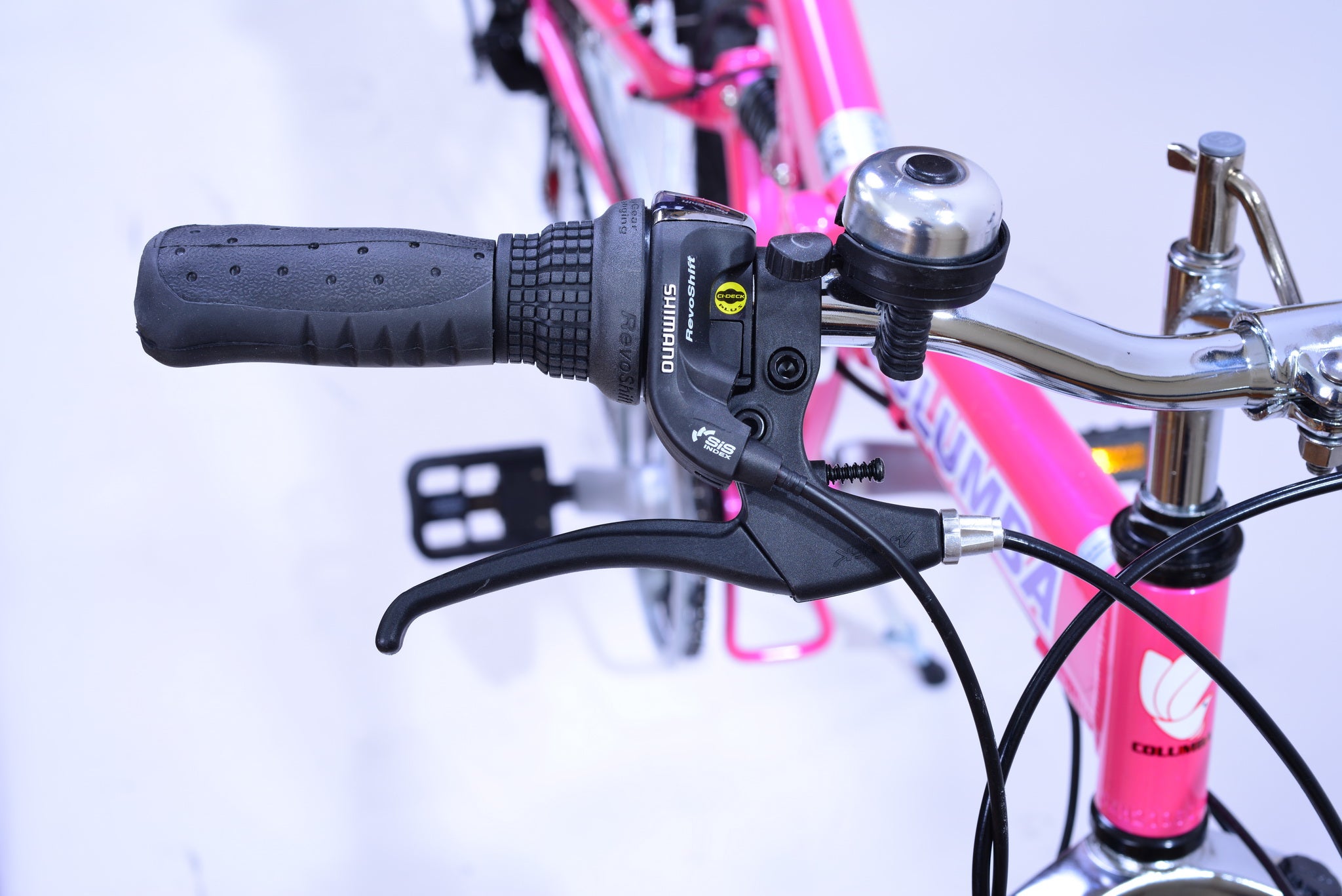 The right handlebar of a bright and vibrant pink bicycle with a bell and brake.