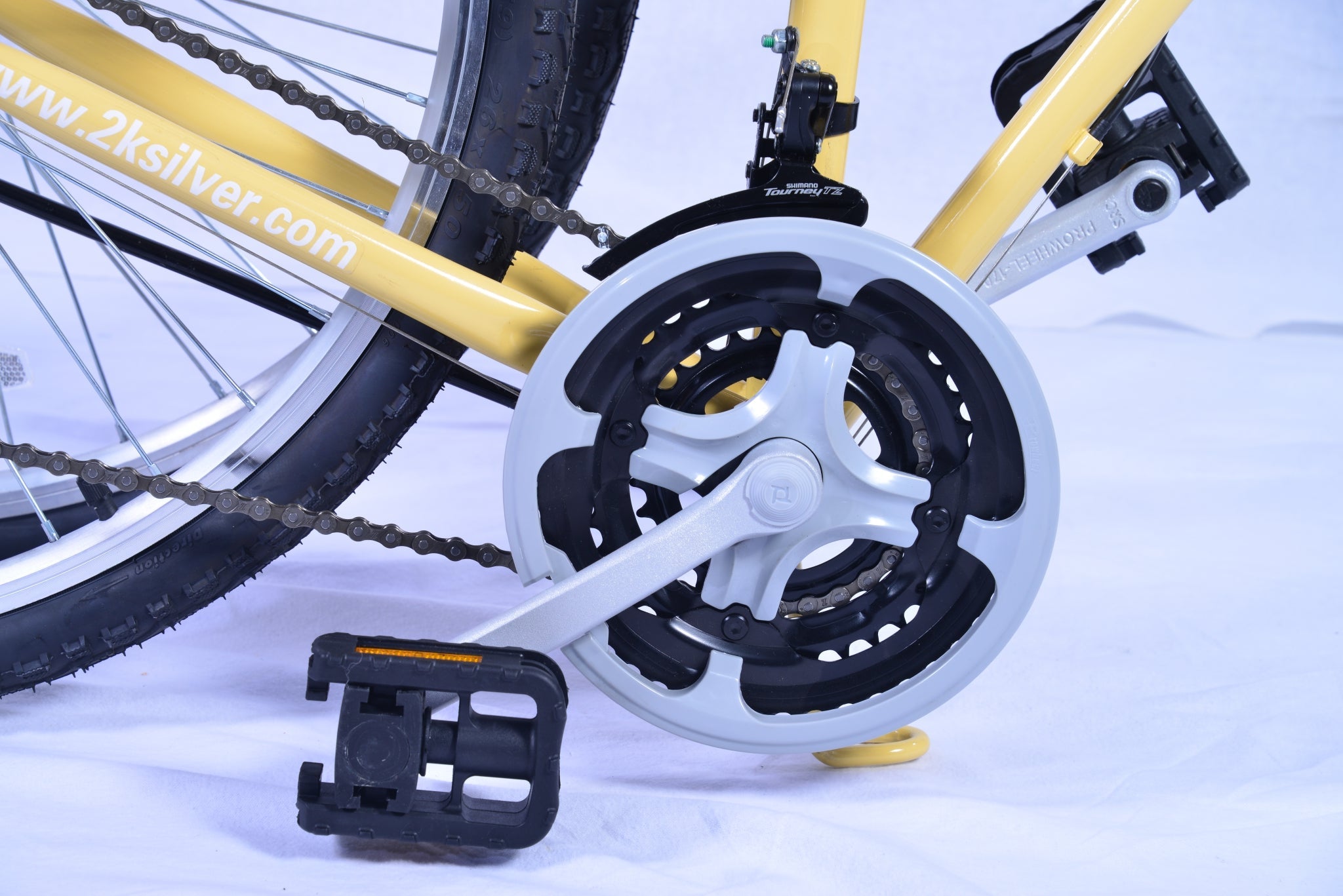 View of a yellow colored bicycle's pedal, crank arm, front derailleur, and chain rings.
