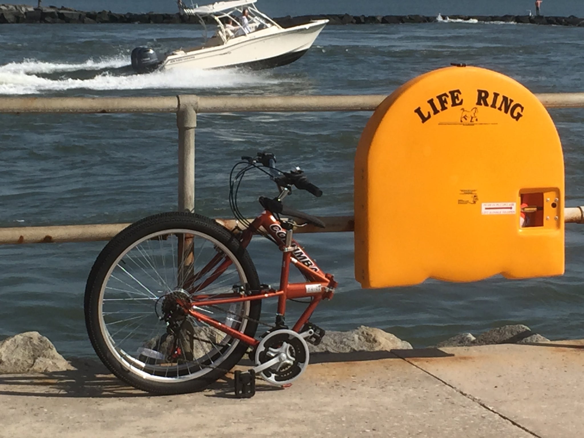 Folded orange bicycle on concrete next to a body of water and a life ring.