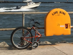 Folded orange bicycle on concrete next to a body of water and a life ring.
