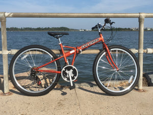 Orange-colored folding bicycle on a pavement outside near water.