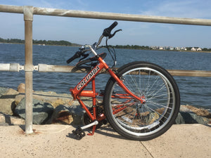An orange folding bicycle in a folded position on a boardwalk next to a body of water.