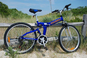 Blue folding bicycle on a sandy beach leaning against a wooden fence.